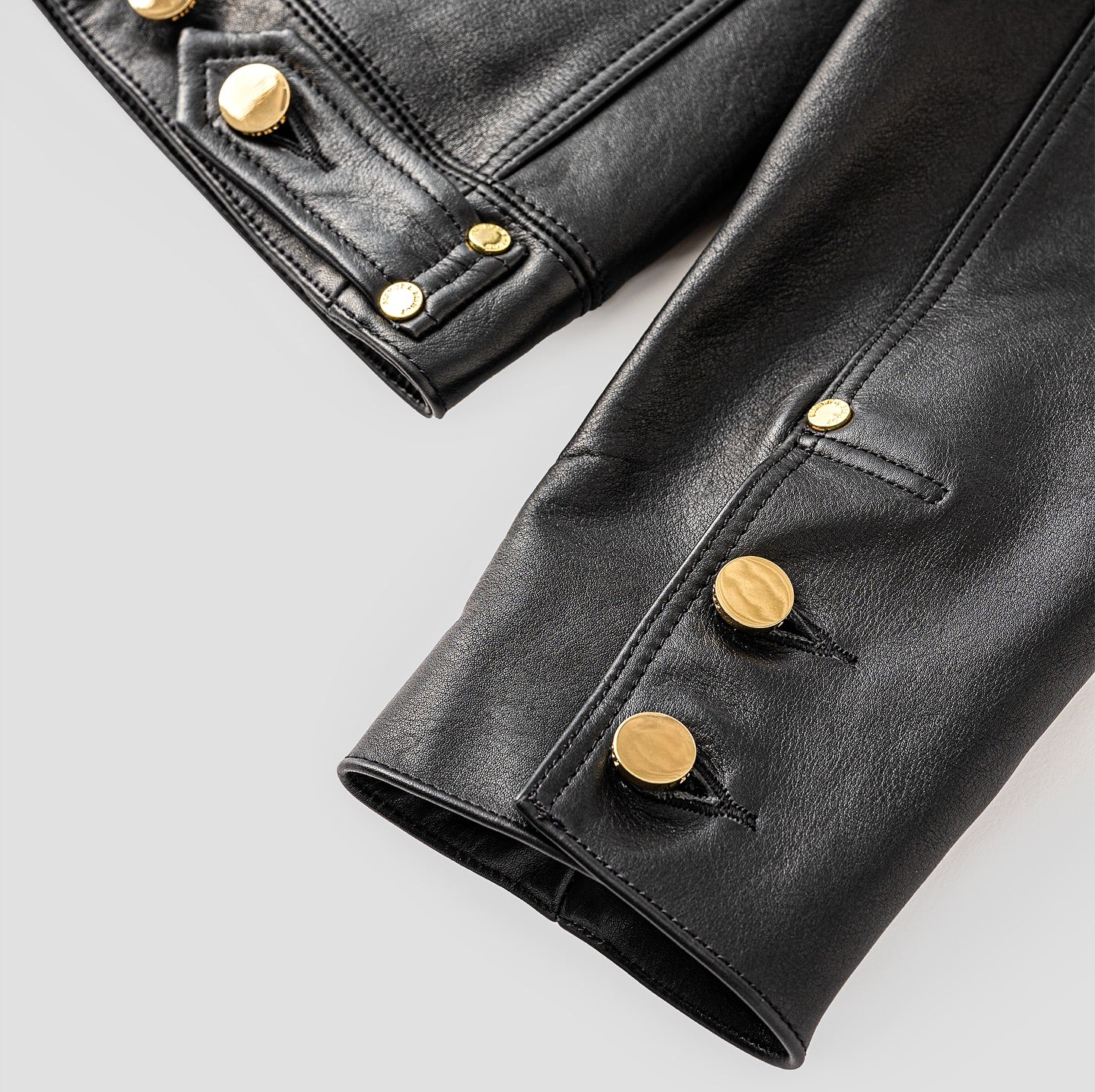 Close-up of a black leather jacket sleeve featuring gold buttons.