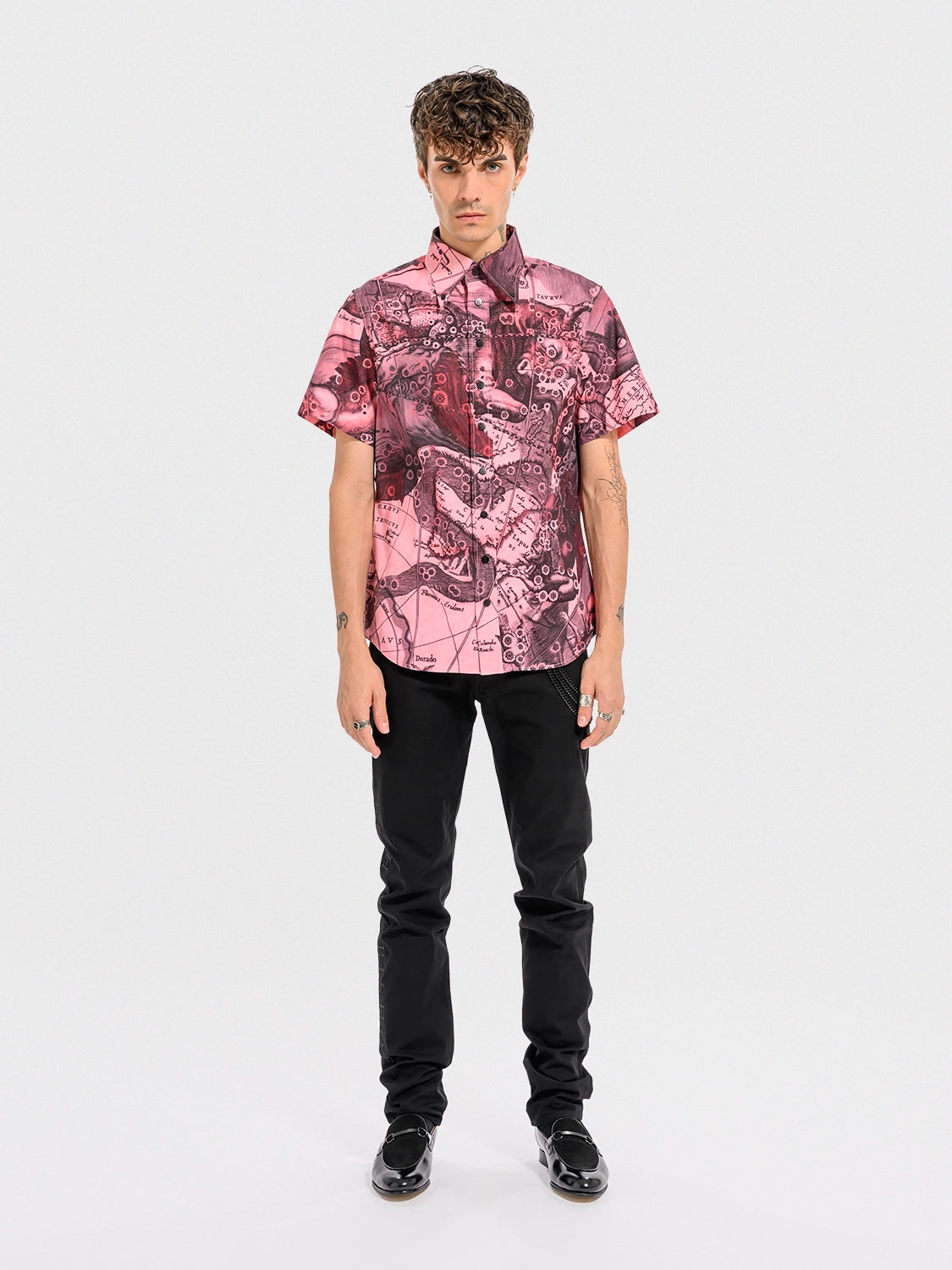 Person wearing a pink patterned shirt and black pants on a white background