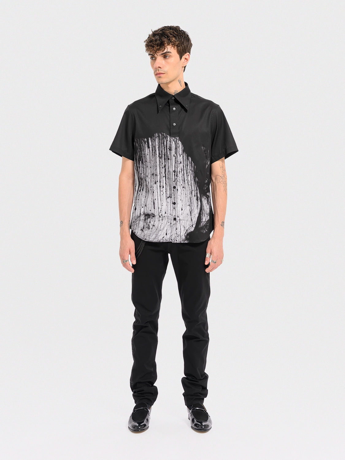 Person wearing a black and white patterned shirt with black pants on a white background
