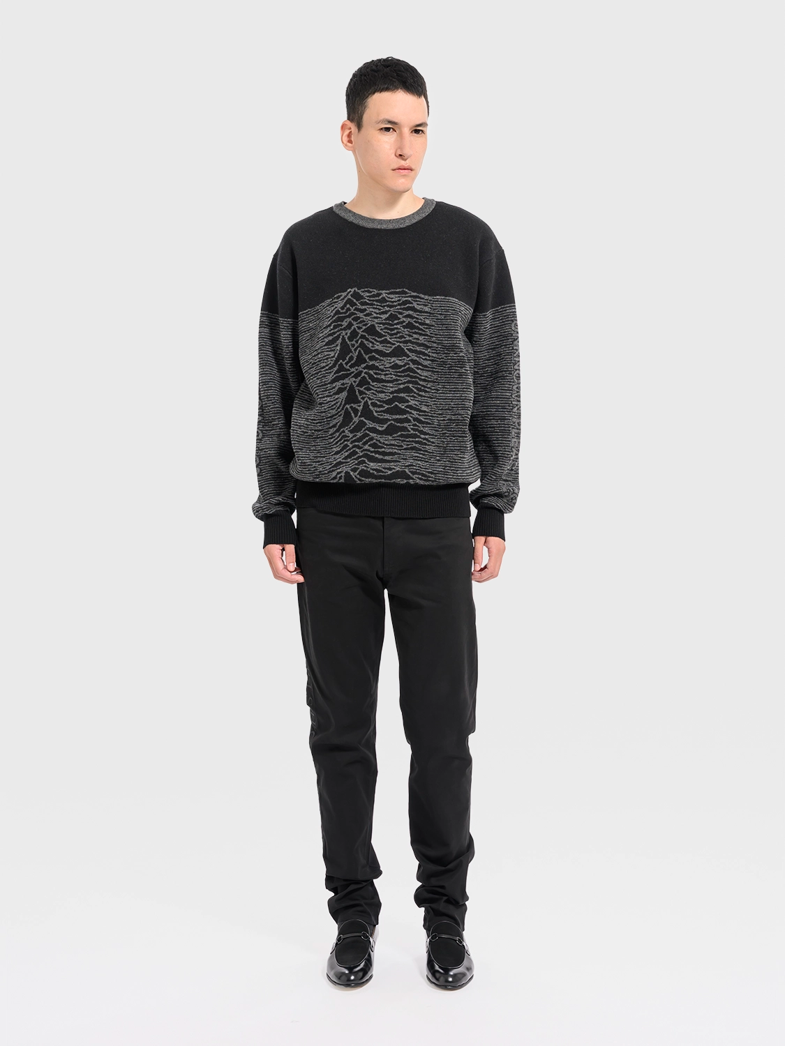 Person wearing a black and gray sweater with a unique pattern on a white background