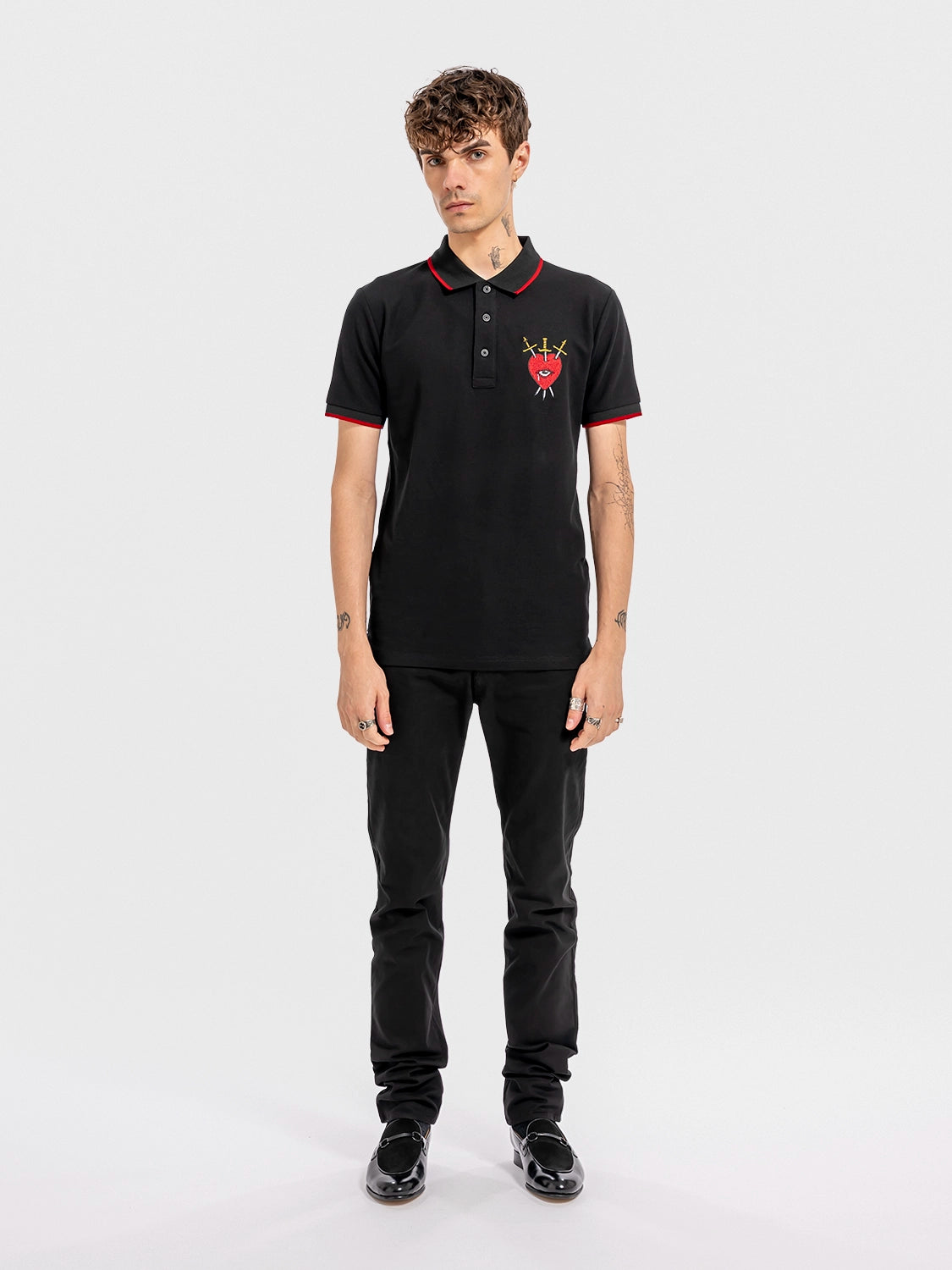 Person wearing a black polo shirt with a graphic print of a red heart, an eye, and crossed swords