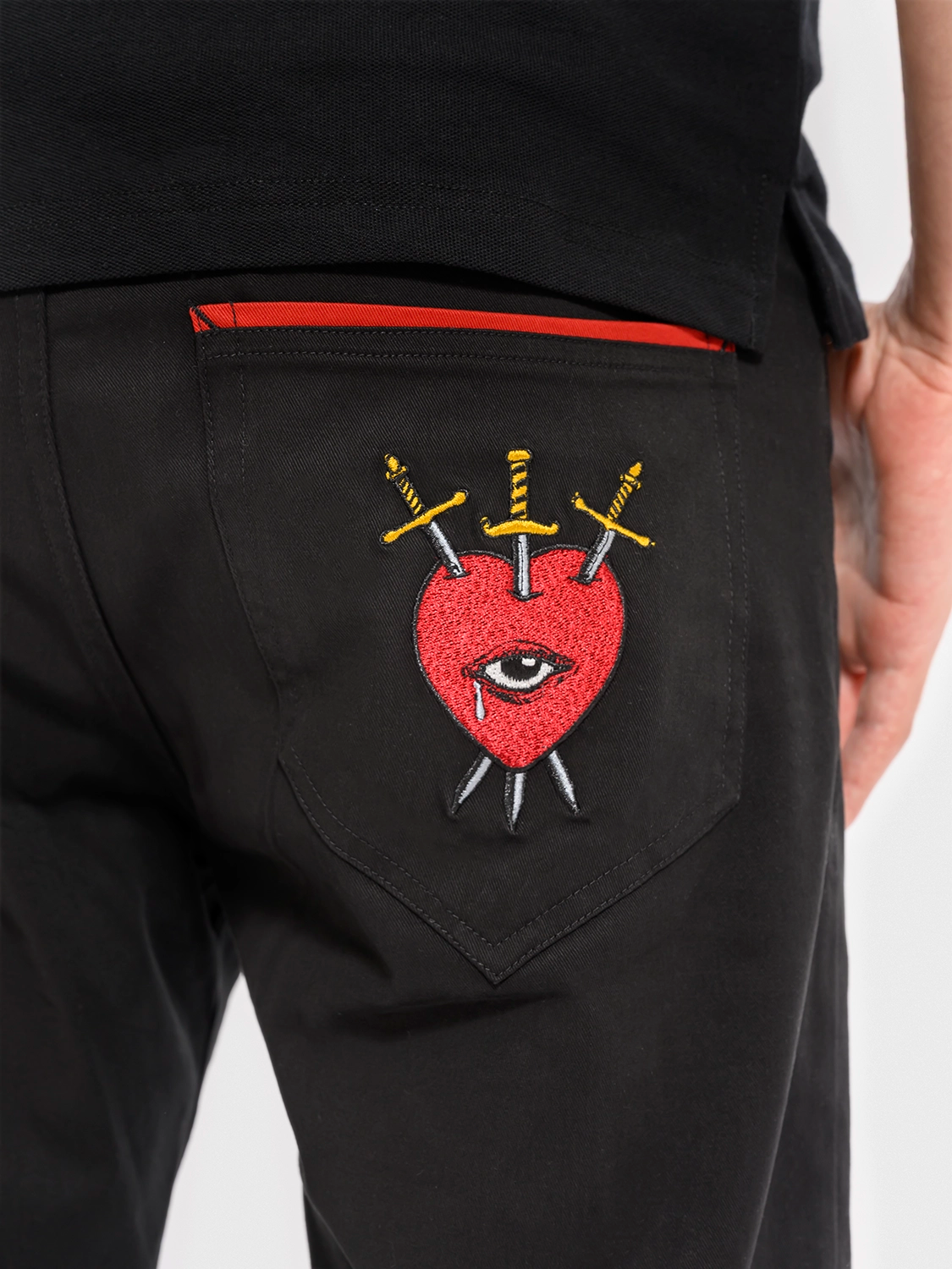 Black cotton pants with a graphic print of a red heart, an eye, and crossed swords