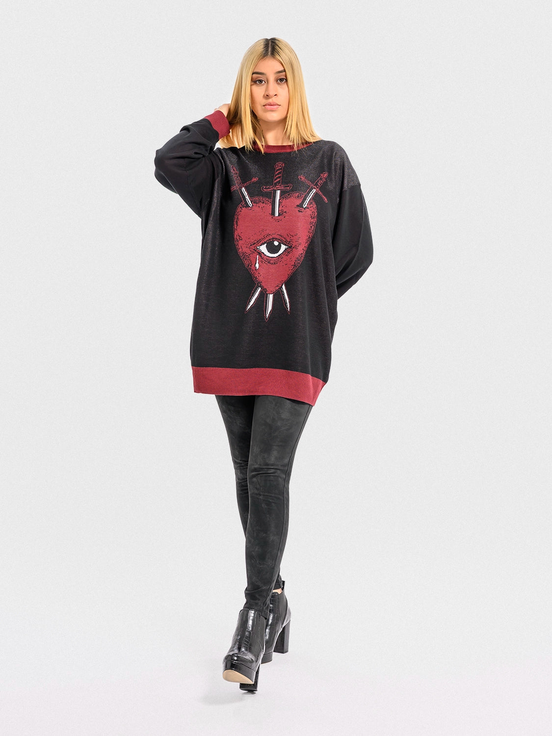 Woman wearing a black sweater with a red heart, an eye, and crossed swords, on a white background