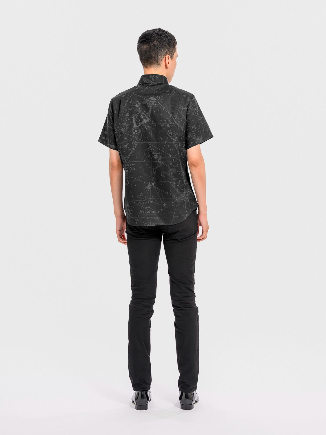 Person wearing a black patterned shirt and black pants on a white background