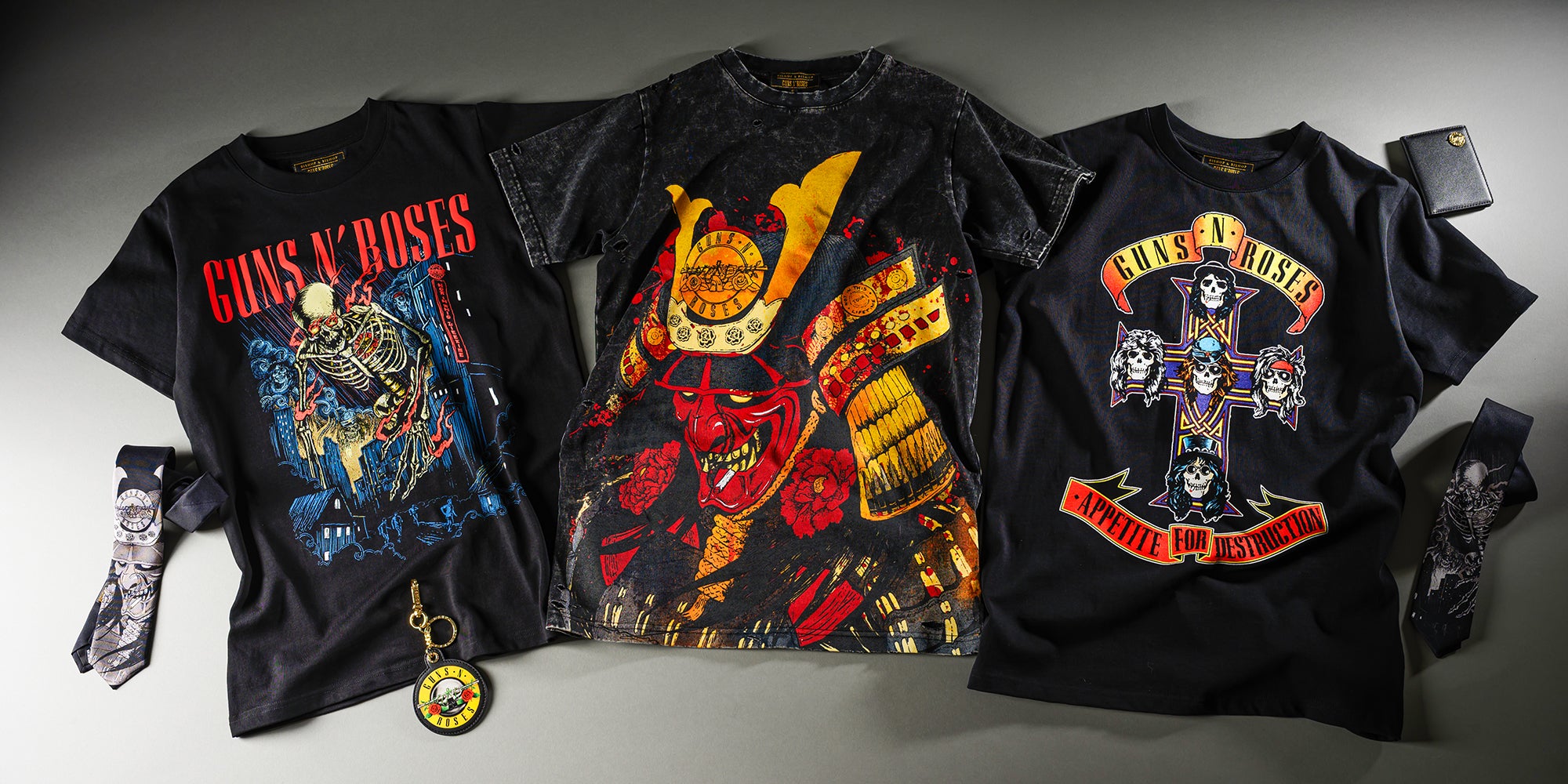 Three black Guns n' Roses t-shirts with colorful graphic designs on a gray surface.