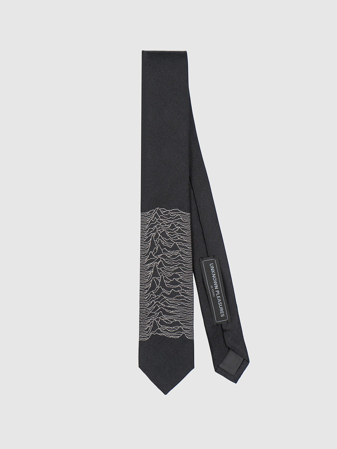 Front view of the black silk tie featuring subtle grey jacquard Unknown Pleasures artwork near the tip.